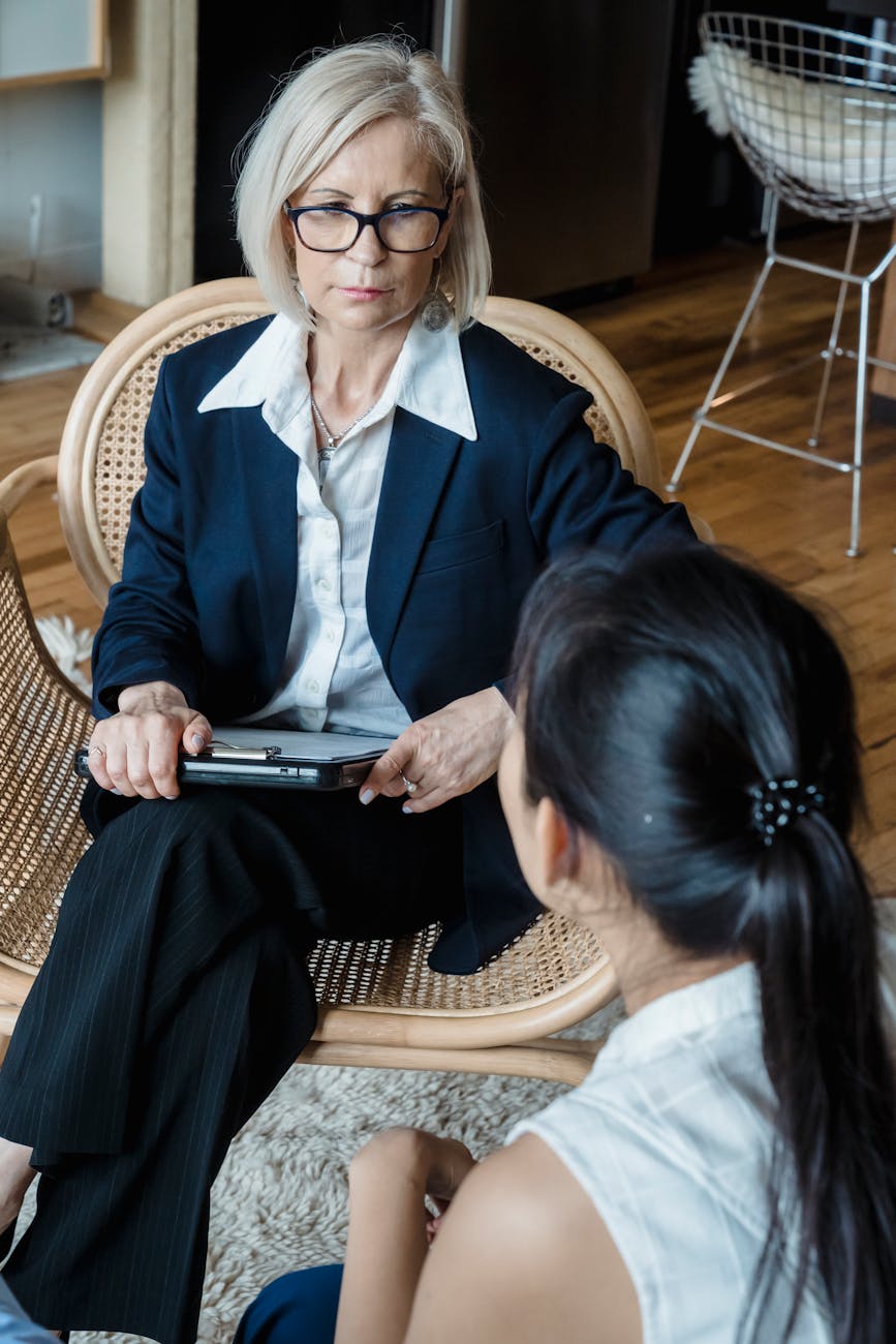 adult woman in dark blue blazer sitting on brown woven chair